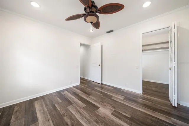 a view of an empty room with wooden floor ceiling fan