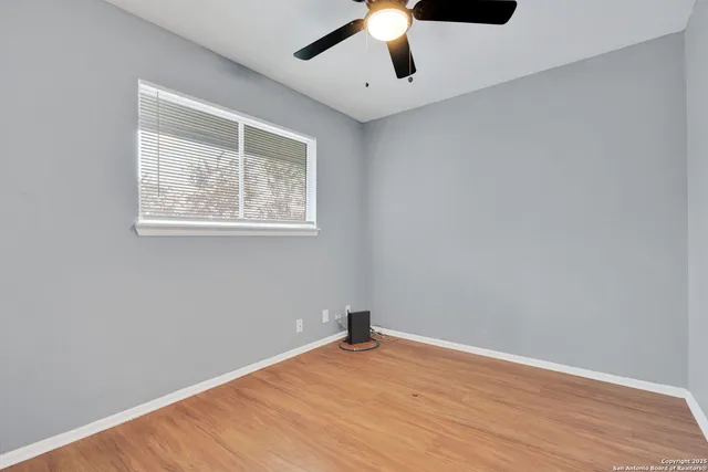 an empty room with wooden floor chandelier fan and windows