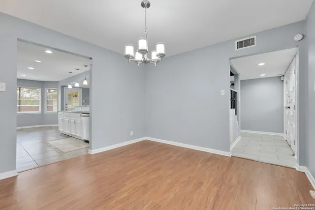 a view of an empty room with wooden floor and a kitchen