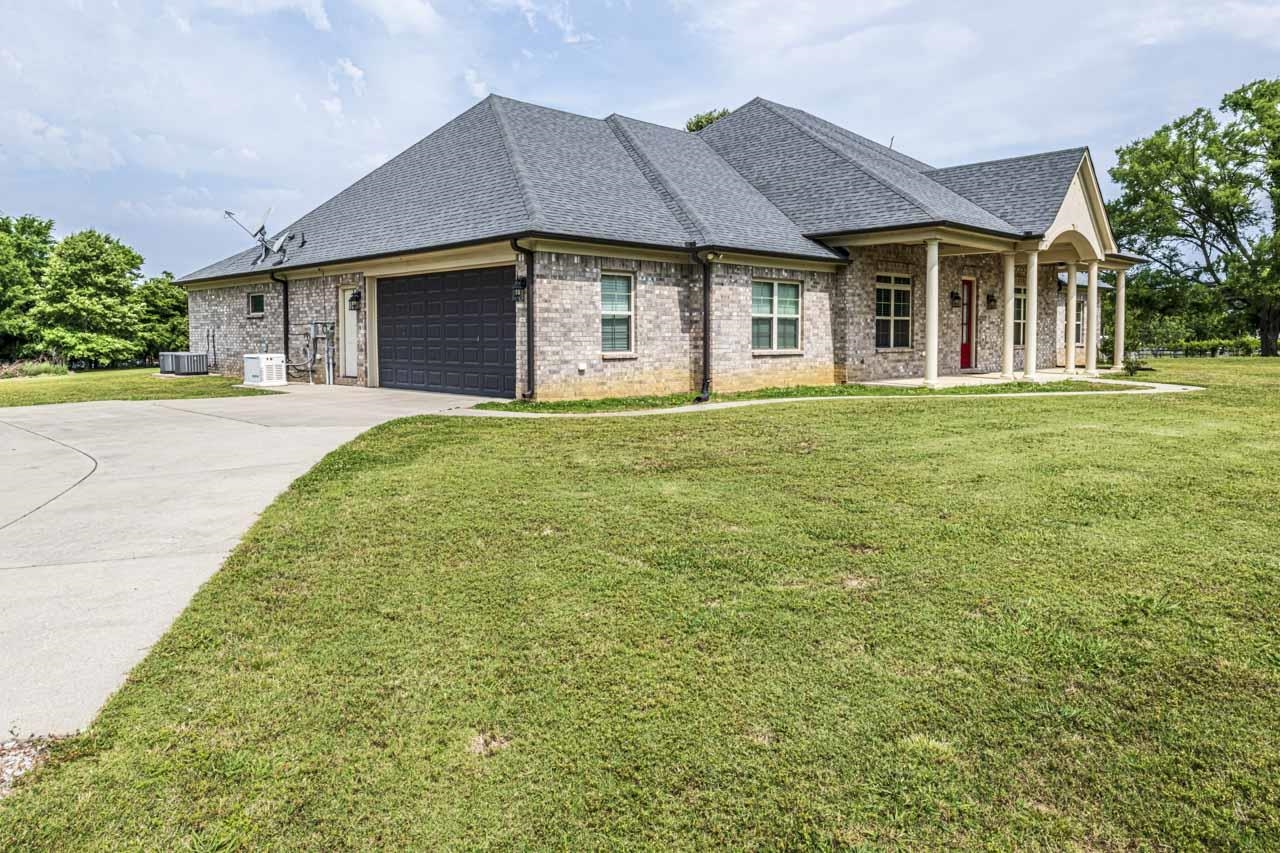 185 Belmont Road Mason, TN 38049 - Photo 35 of 38 Light-colored brick exterior featuring a dark gray shingle roof, attached garage with a dark gray door, and a covered front porch with columns and a red front door
