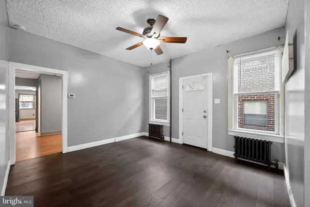 an empty room with wooden floor fan and windows