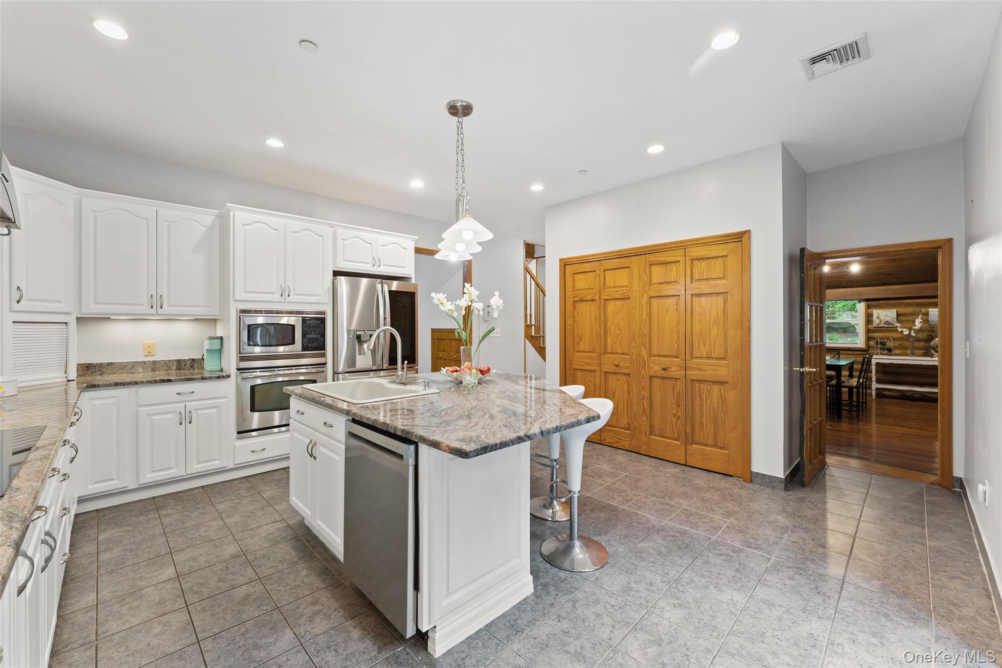 25 Cabin Ridge Road Chappaqua, NY 10514 - Photo 14 of 39 Well-appointed kitchen featuring a central island with an integrated sink and breakfast bar, white cabinetry, stainless steel appliances, recessed lighting, and tiled flooring