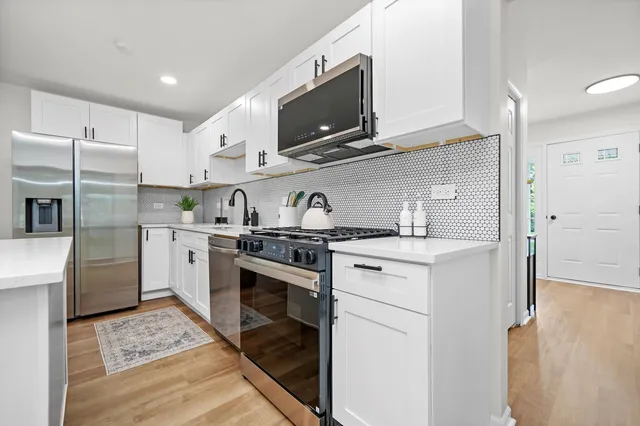 a kitchen with stainless steel appliances granite countertop a sink stove a refrigerator and white cabinets with wooden floor