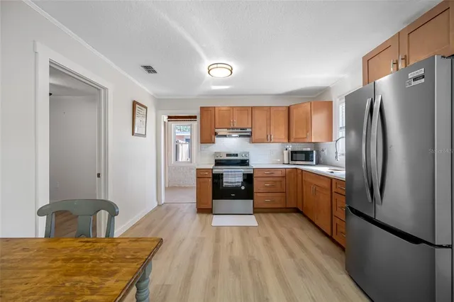 a kitchen with stainless steel appliances granite countertop a refrigerator a stove top oven a sink dishwasher and white cabinets with wooden floor