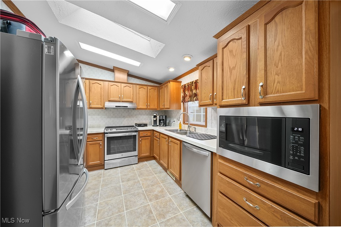 17296 Old State Road Middlefield, OH 44062 - Photo 14 of 44 Kitchen featuring lofted ceiling with skylight, backsplash, sink, light tile patterned floors, and appliances with stainless steel finishes