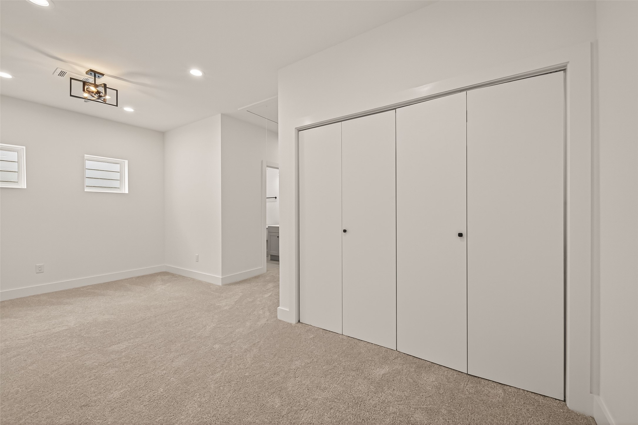 6808 Madrid Street Houston, TX 77021 - Photo 17 of 31 This photo showcases a spacious, modern bedroom with neutral carpet, ample closet space, and contemporary lighting. The room has a clean, minimalist design with two small windows for natural light.