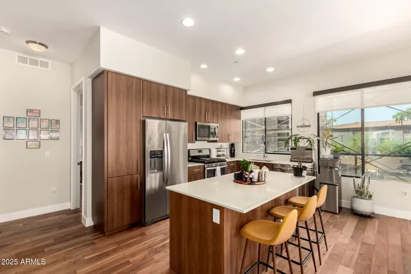 a kitchen with stainless steel appliances a refrigerator a stove a sink a dining table and chairs with wooden floor