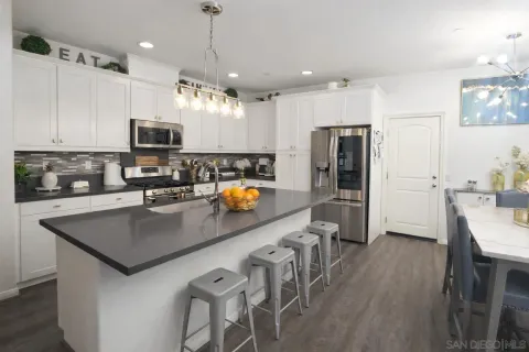 a kitchen with stainless steel appliances a refrigerator a stove a sink a dining table and chairs with wooden floor