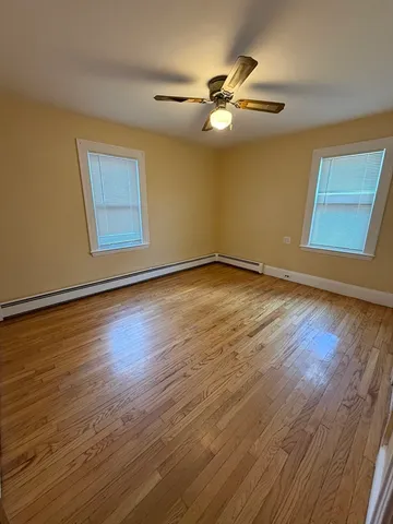 a view of an empty room with wooden floor and a ceiling fan