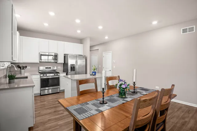 a kitchen with stainless steel appliances granite countertop a stove top oven a dining table and chairs with wooden floor