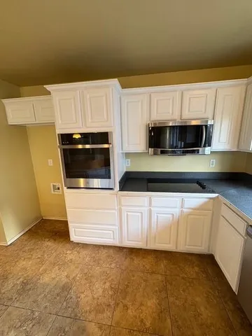 a kitchen with granite countertop a refrigerator a sink and white cabinets