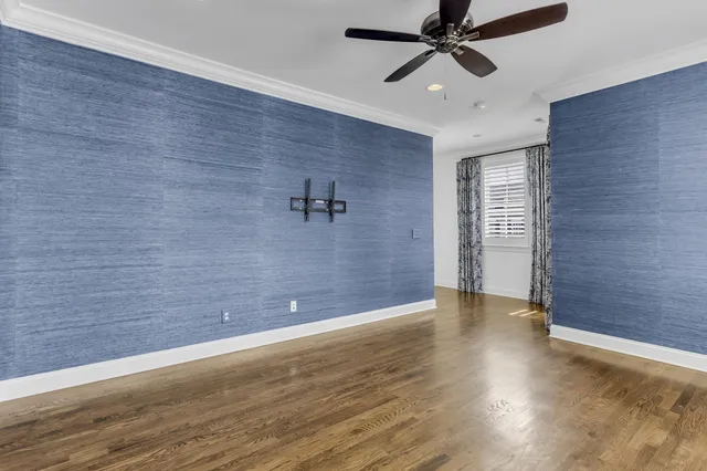 an empty room with wooden floor chandelier fan and windows