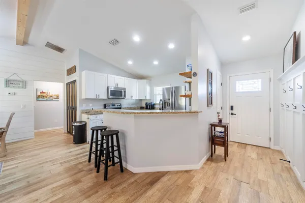 a living room with stainless steel appliances kitchen island granite countertop a refrigerator a stove top oven and wooden floors