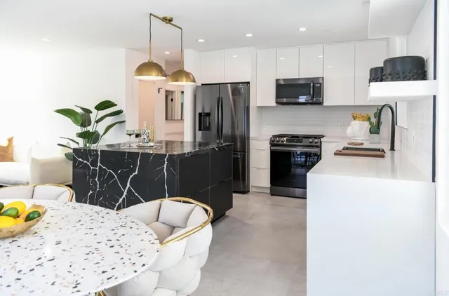 a kitchen with stainless steel appliances kitchen island granite countertop a sink a stove a refrigerator a microwave oven with white cabinets and wooden floor