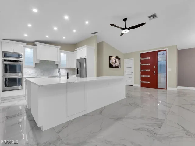 a large white kitchen with kitchen island a sink stainless steel appliances and cabinets