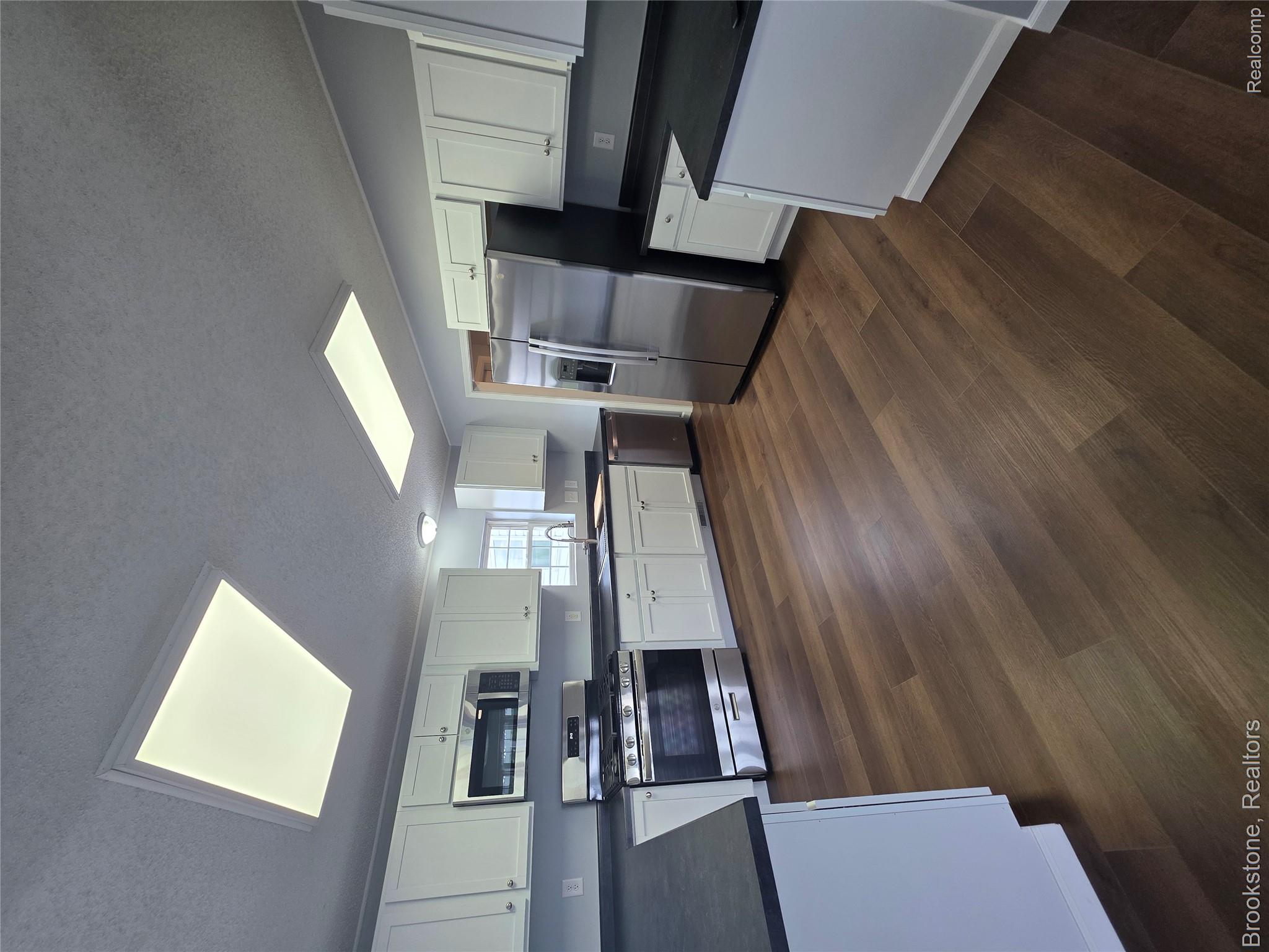 4064 East Wilson Road Clio, MI 48420 - Photo 9 of 23 Kitchen featuring dark wood-finish flooring, white cabinetry, dark countertops, and stainless steel appliances