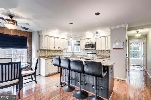 a kitchen with stainless steel appliances granite countertop a stove a refrigerator a kitchen island a dining table and chairs with wooden floor