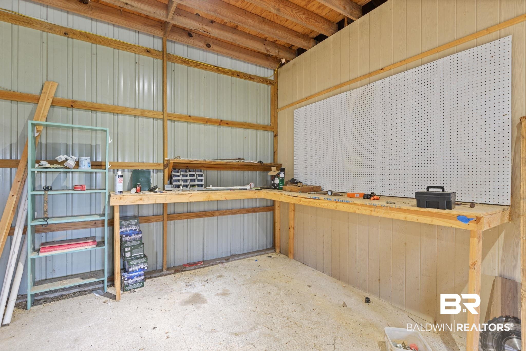 7540 2 Mile Road Irvington, AL 36544 - Photo 71 of 82 Workstation featuring a built-in wooden workbench, integrated pegboard, exposed wood beam ceiling, corrugated metal wall panels, and a concrete floor