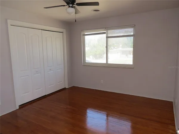 an empty room with wooden floor fan and windows