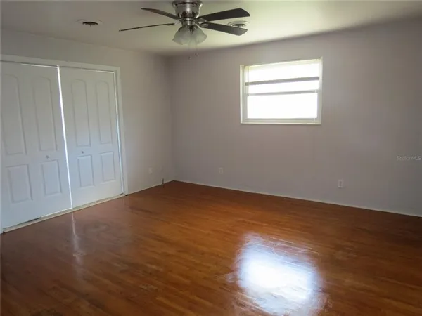 an empty room with wooden floor fan and windows