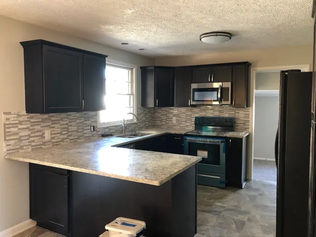 a kitchen with granite countertop a refrigerator a stove a sink a counter space and cabinets