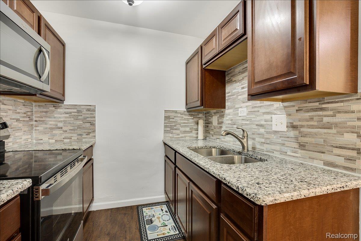 22444 Kelly Road, Unit 11 Eastpointe, MI 48021 - Photo 7 of 13 Kitchen featuring stainless steel appliances, light stone counters, tasteful backsplash, and dark wood-type flooring