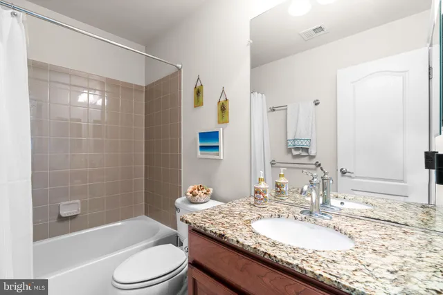 a bathroom with a granite countertop sink a toilet a mirror a bathtub and shower