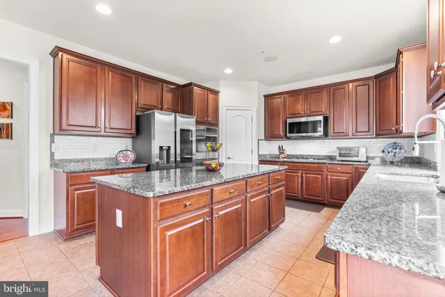 a kitchen with stainless steel appliances granite countertop a stove top oven a sink dishwasher a microwave oven and a refrigerator with wooden cabinets