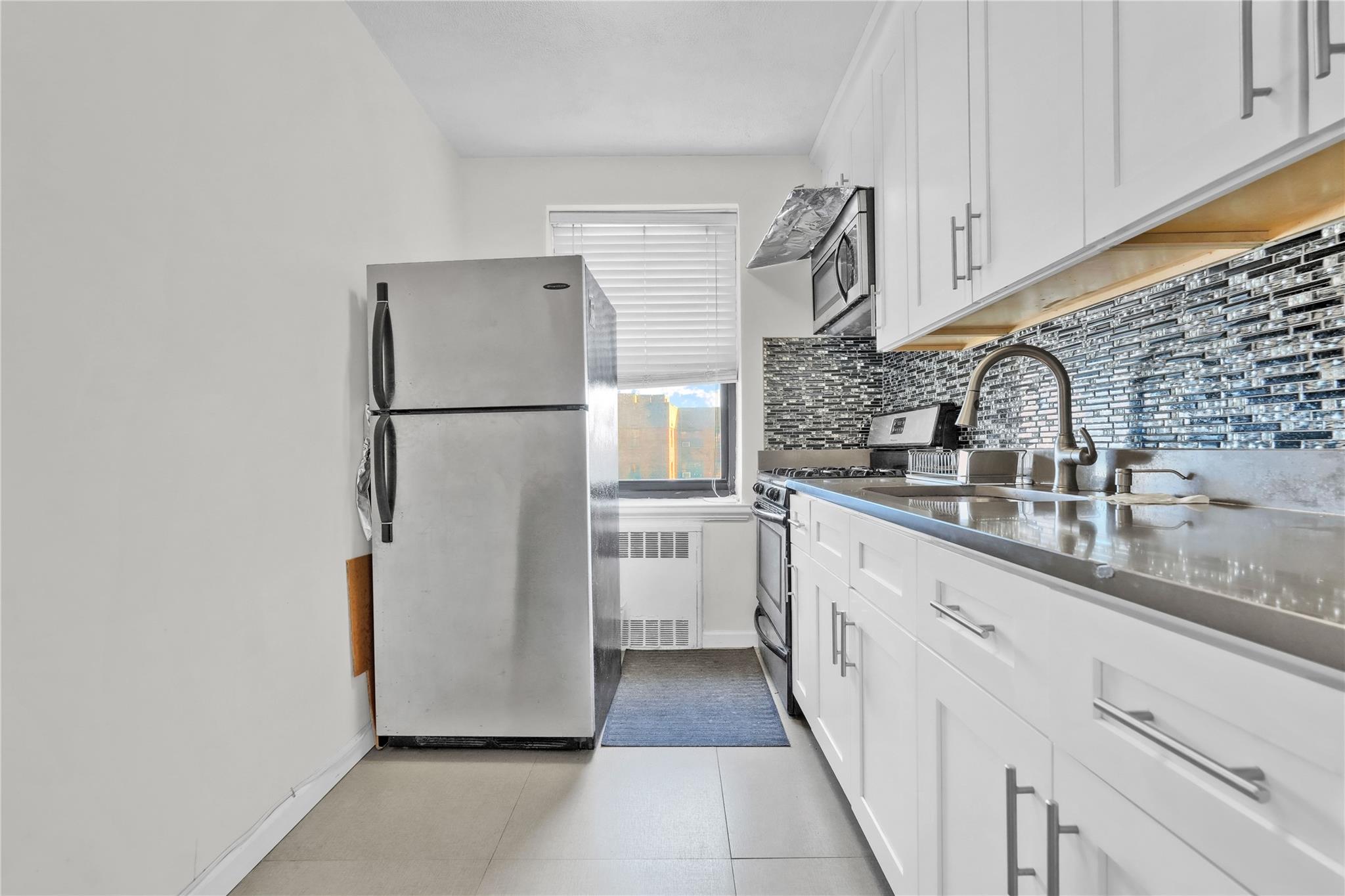 139-09 28th Road, Unit 6F Queens, NY 11354 - Photo 9 of 14 Kitchen with appliances with stainless steel finishes, radiator, tasteful backsplash, white cabinets, and dark countertops