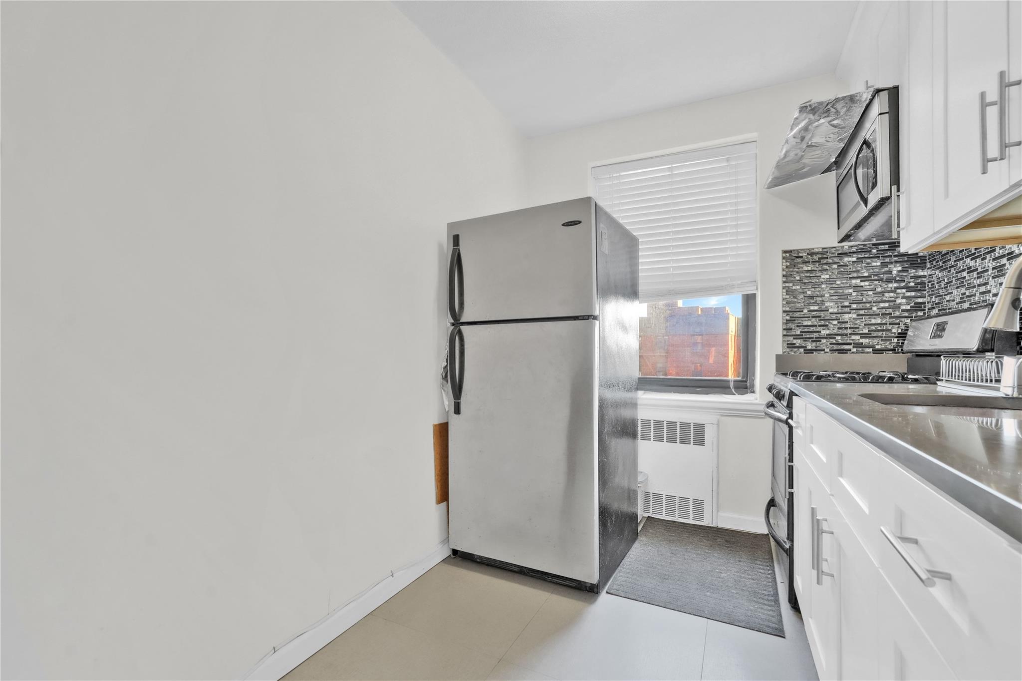 139-09 28th Road, Unit 6F Queens, NY 11354 - Photo 10 of 14 Kitchen featuring appliances with stainless steel finishes, radiator, decorative backsplash, and white cabinetry