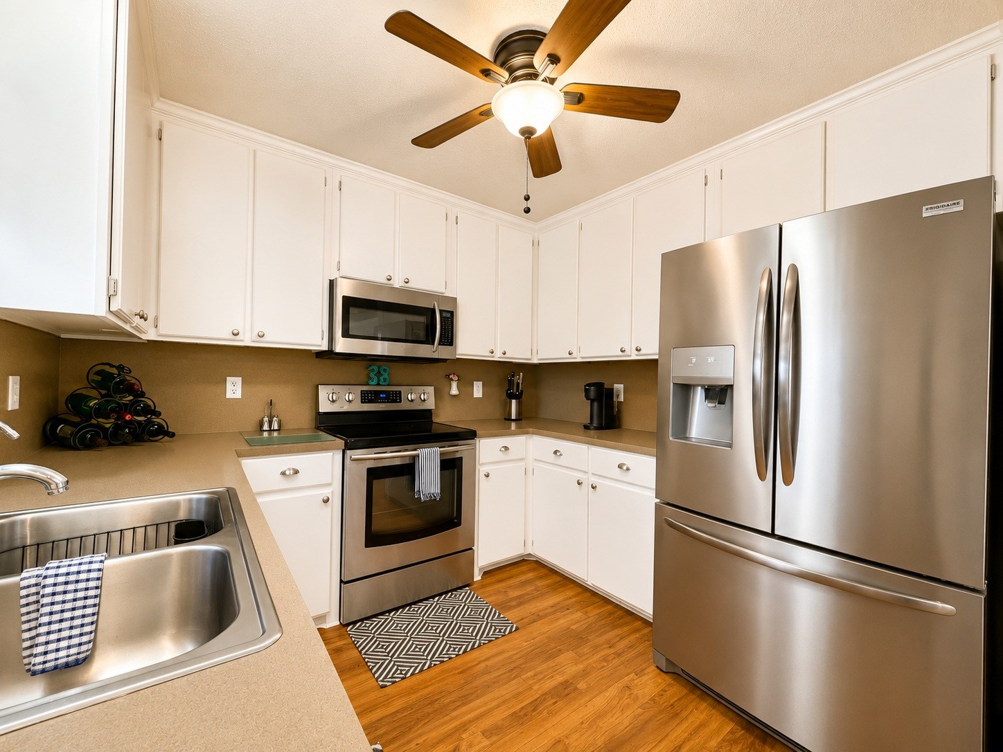 135 Sand Shoals Road Freeport, TX 77541 - Photo 9 of 20 Modern kitchen with stainless steel appliances, white cabinetry, and wood flooring. Features a ceiling fan, ample counter space, and a convenient layout.