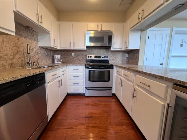 a white kitchen with granite top and stainless steel appliances