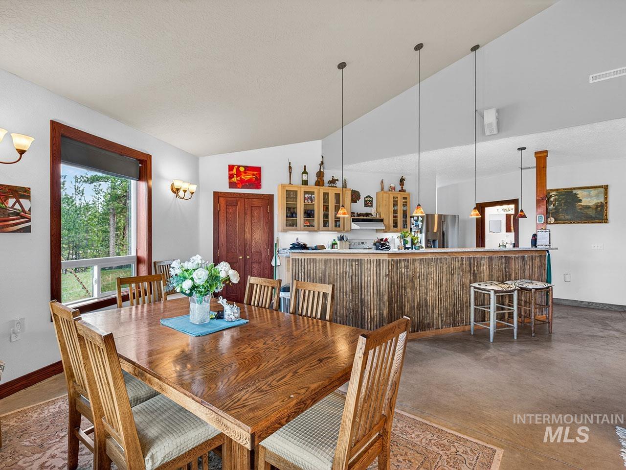 10885 Callender Road Cascade, ID 83611 - Photo 14 of 31 Vaulted ceiling dining area featuring a wood-finish dining table, large window with wood-finish trim, and wall sconce lighting
