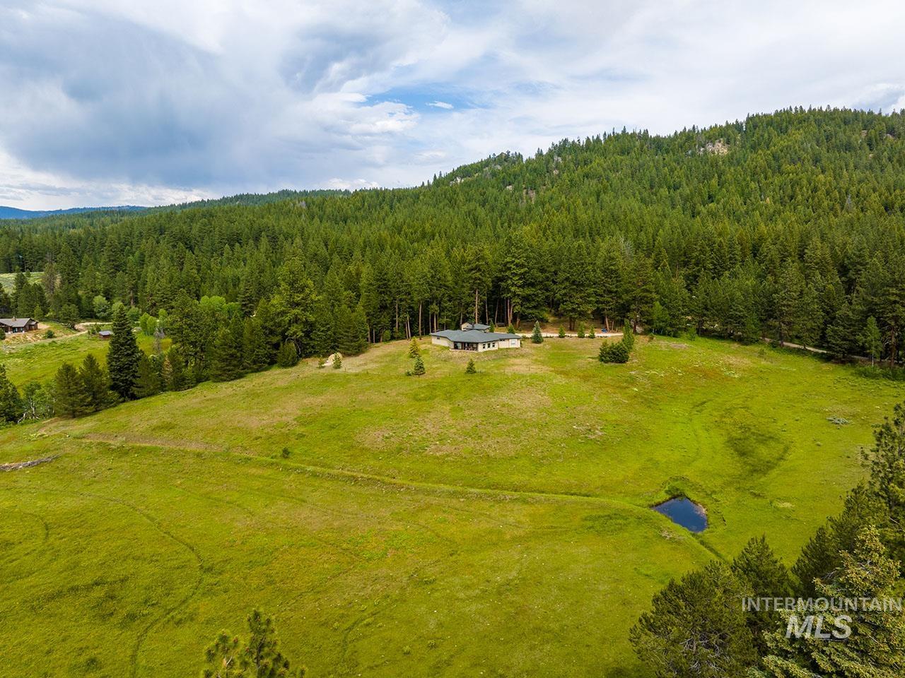 10885 Callender Road Cascade, ID 83611 - Photo 2 of 31 Expansive green acreage featuring a single-story residence with a dark roof, surrounded by mature evergreen trees