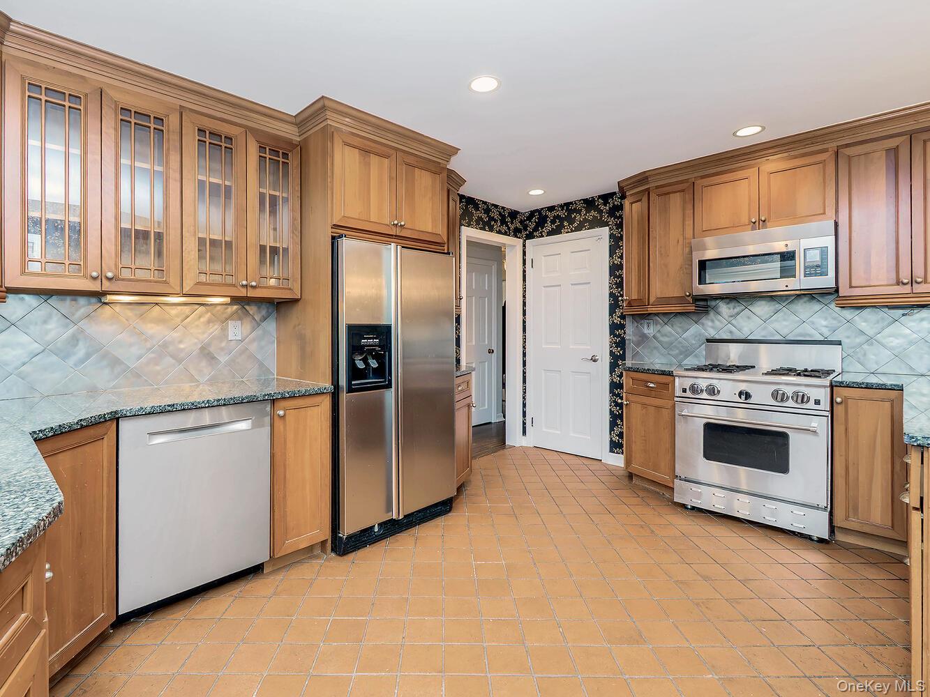 41 South 4th Street Locust Valley, NY 11560 - Photo 12 of 39 Kitchen featuring dark stone counters, backsplash, appliances with stainless steel finishes, brown cabinetry, and recessed lighting