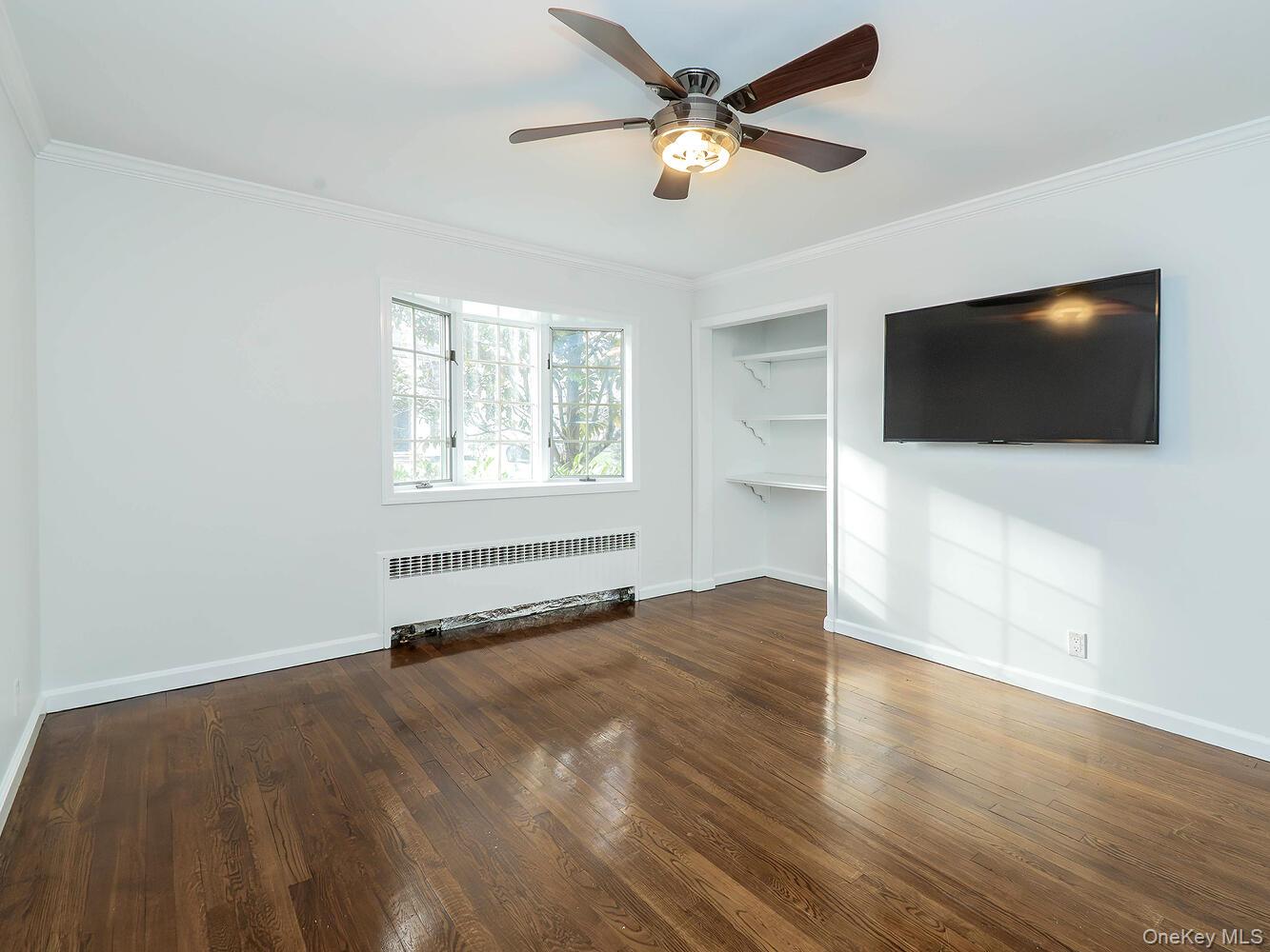 41 South 4th Street Locust Valley, NY 11560 - Photo 15 of 39 Unfurnished living room featuring crown molding, radiator, built in shelves, dark wood-type flooring, and ceiling fan