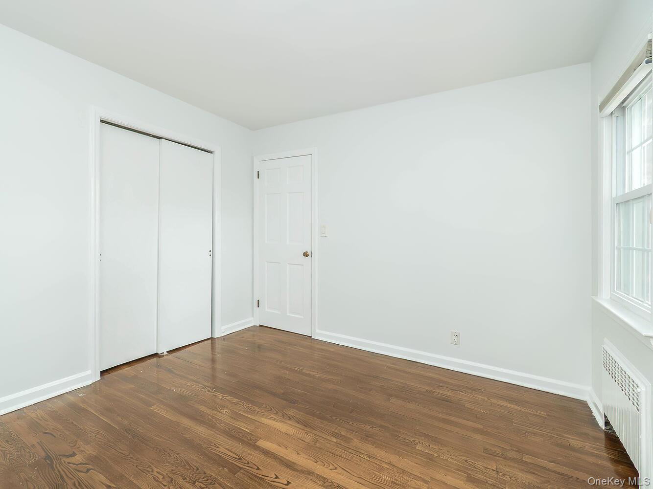 41 South 4th Street Locust Valley, NY 11560 - Photo 23 of 39 Unfurnished bedroom featuring radiator, dark wood-style floors, and a closet