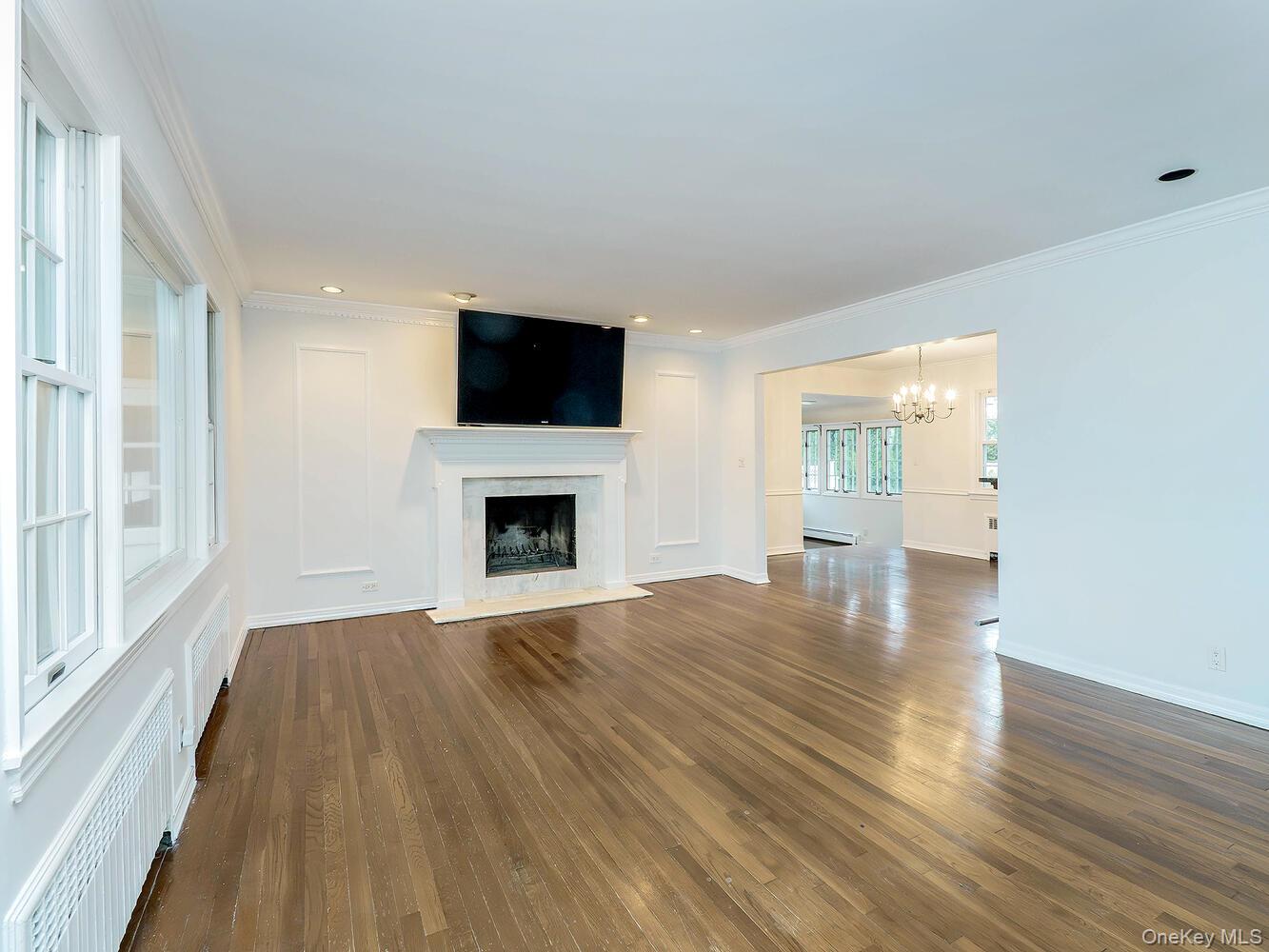 41 South 4th Street Locust Valley, NY 11560 - Photo 4 of 39 Unfurnished living room featuring radiator, dark wood-style floors, crown molding, a premium fireplace, and a chandelier