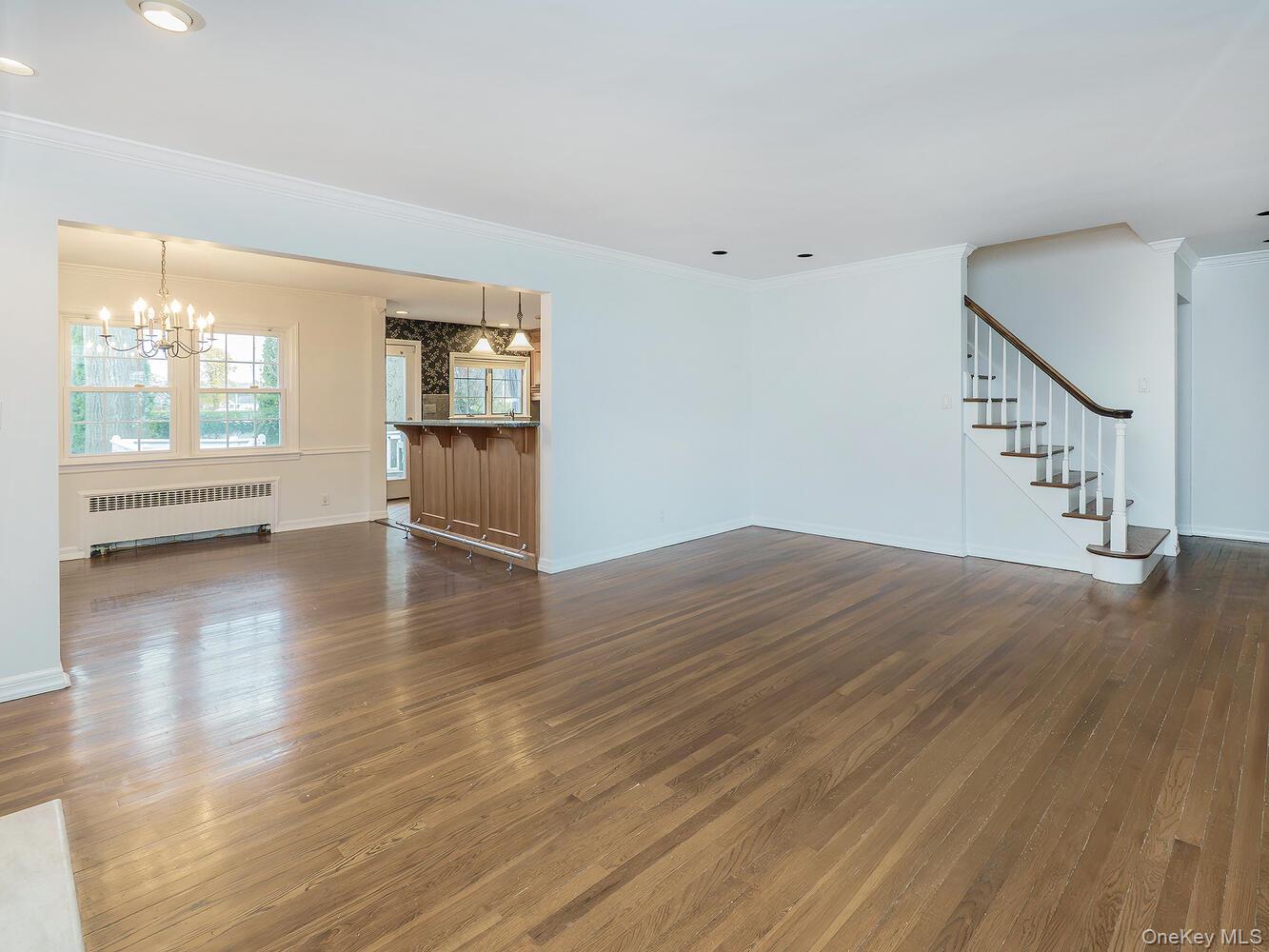 41 South 4th Street Locust Valley, NY 11560 - Photo 5 of 39 Unfurnished living room featuring radiator, crown molding, stairway, dark wood finished floors, and a chandelier