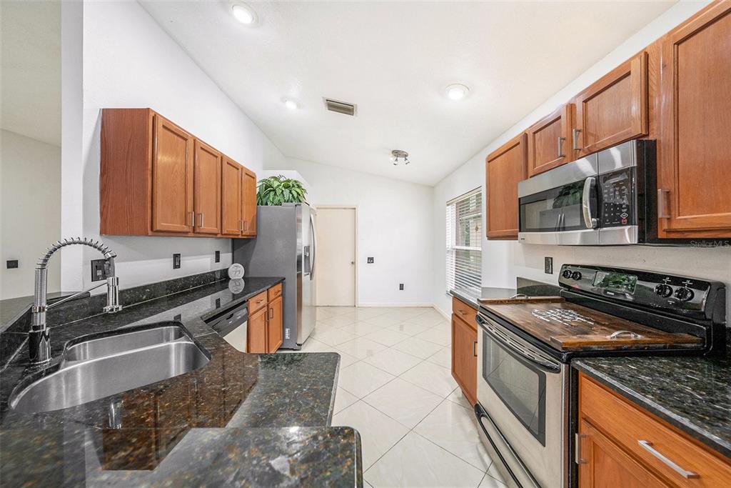 5644 Grindstone Loop Wesley Chapel, FL 33544 - Photo 13 of 29 a kitchen with stainless steel appliances granite countertop a stove a sink and a microwave