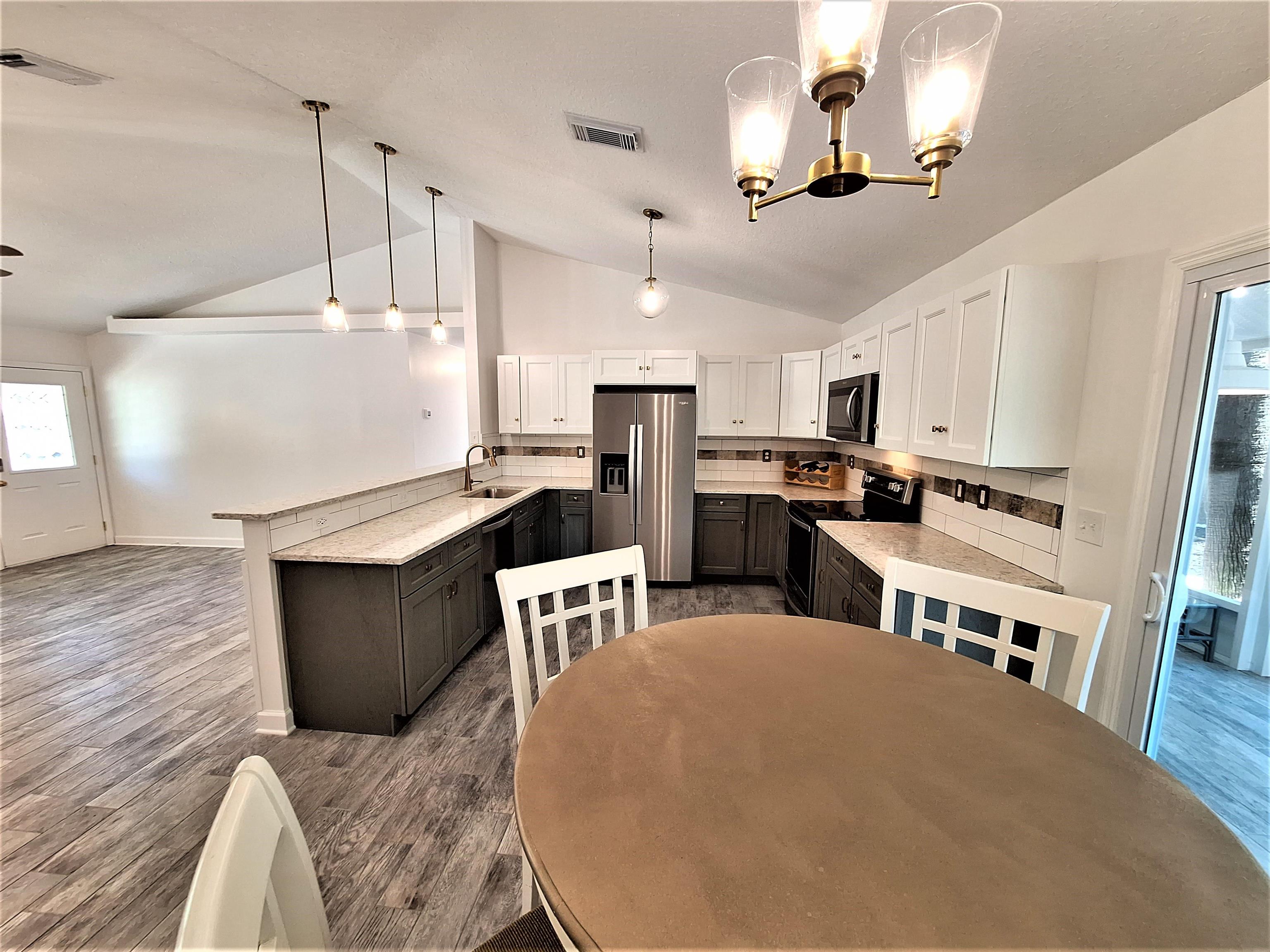 129 15th Street St. Augustine, FL 32080 - Photo 43 of 61 a kitchen with stainless steel appliances kitchen island granite countertop a refrigerator a stove top oven a sink dishwasher and white cabinets with wooden floor