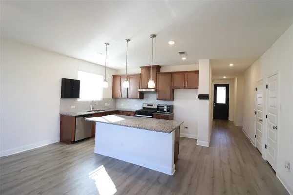 a kitchen with stainless steel appliances granite countertop a stove top oven a sink dishwasher and a refrigerator with wooden floor