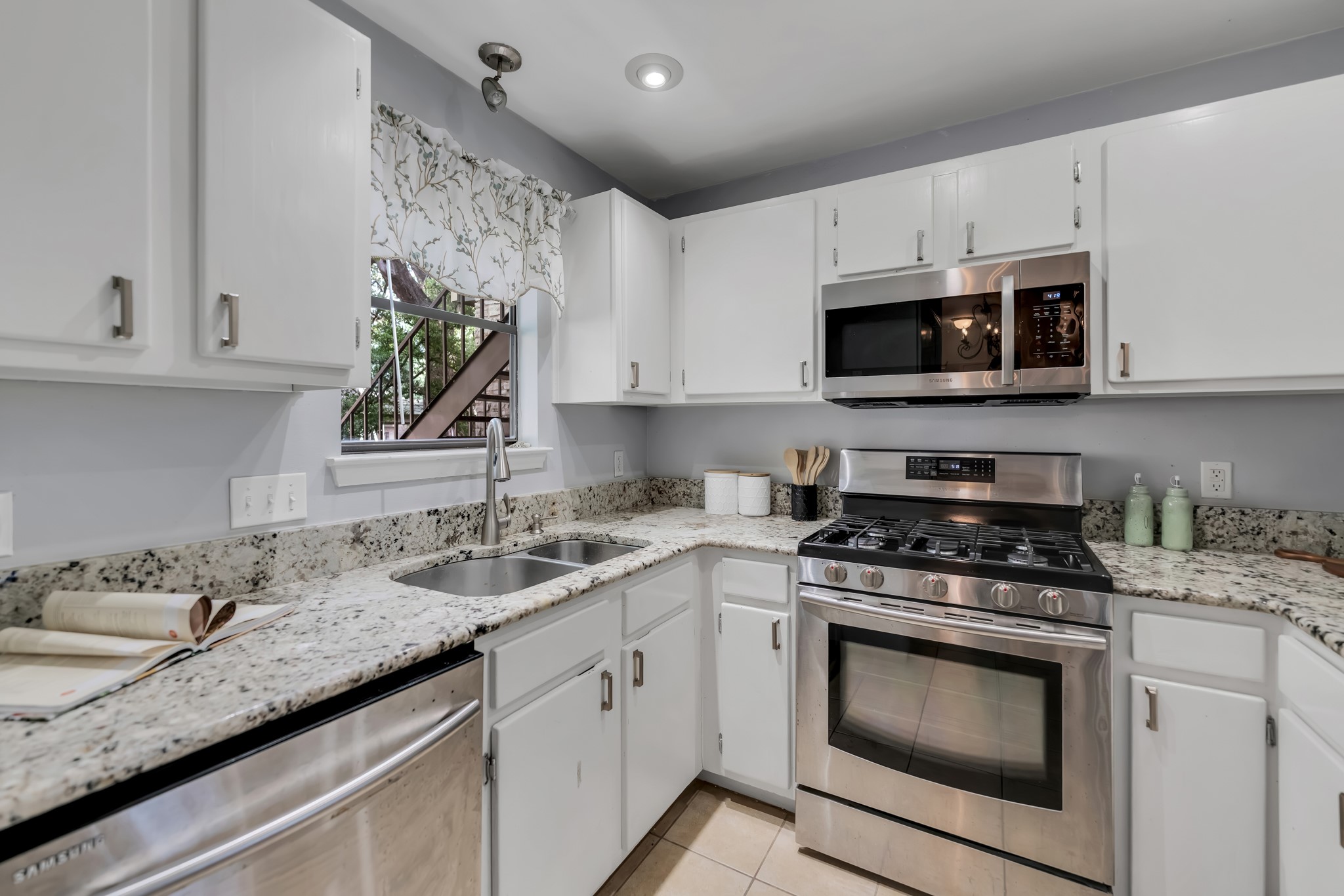 11970 Jollyville Road, Unit 104 Austin, TX 78759 - Photo 5 of 22 The kitchen features white cabinetry, granite countertops, and stainless steel appliances including a gas range, microwave, and dishwasher