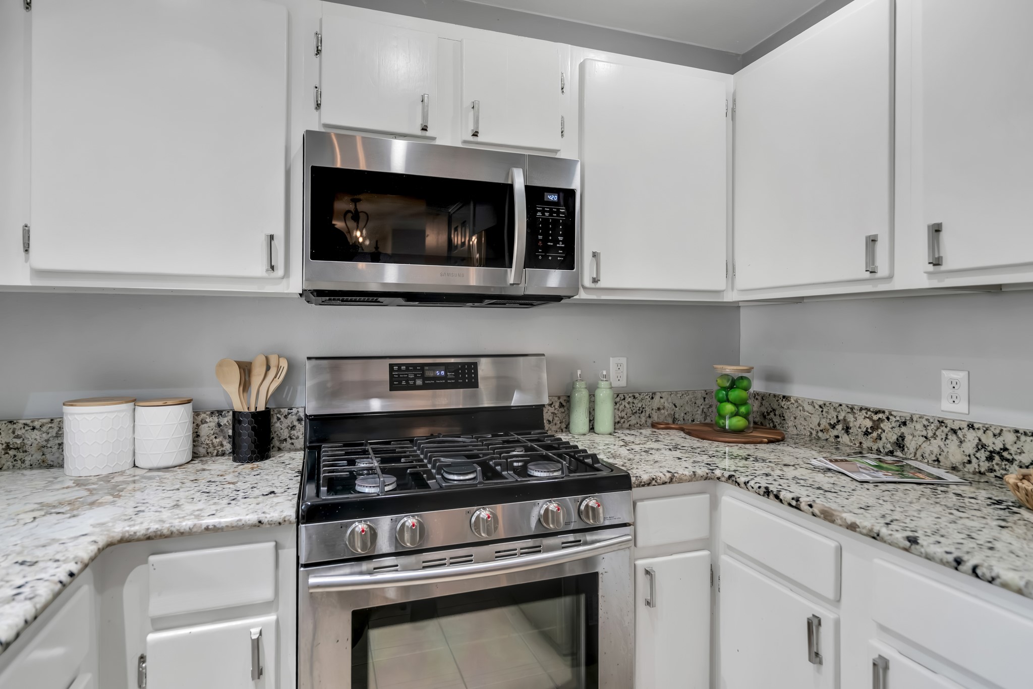 11970 Jollyville Road, Unit 104 Austin, TX 78759 - Photo 6 of 22 The kitchen features white cabinetry, granite countertops, and stainless steel appliances including a microwave and a gas range
