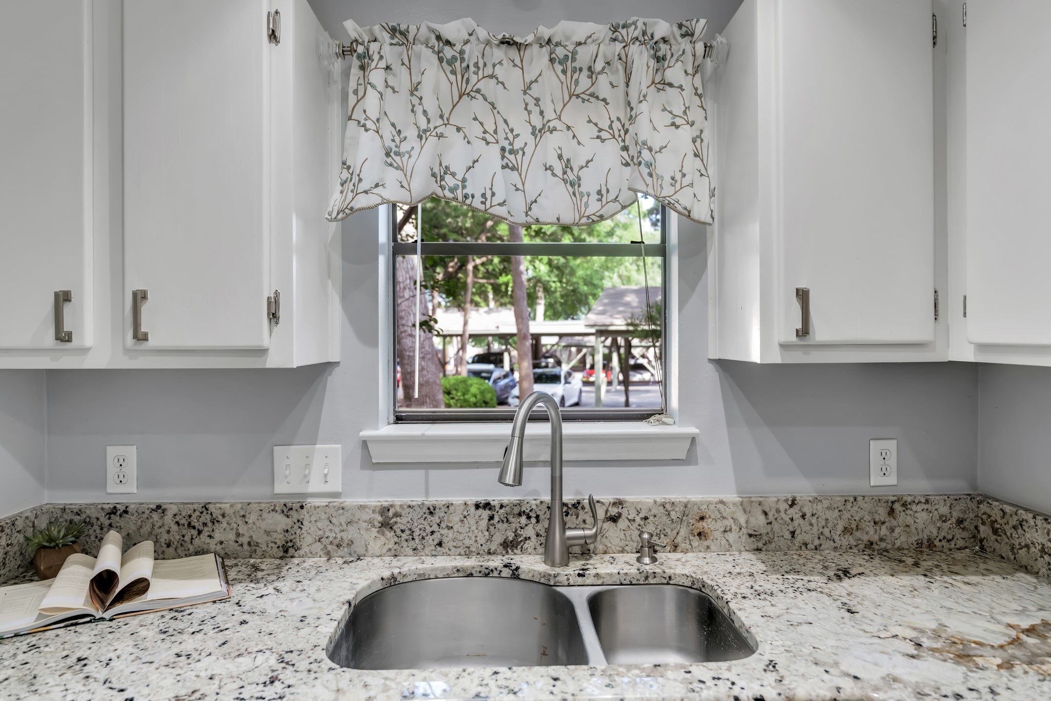 11970 Jollyville Road, Unit 104 Austin, TX 78759 - Photo 7 of 22 The kitchen features granite countertops, a stainless steel double basin sink, and white cabinetry with brushed nickel hardware