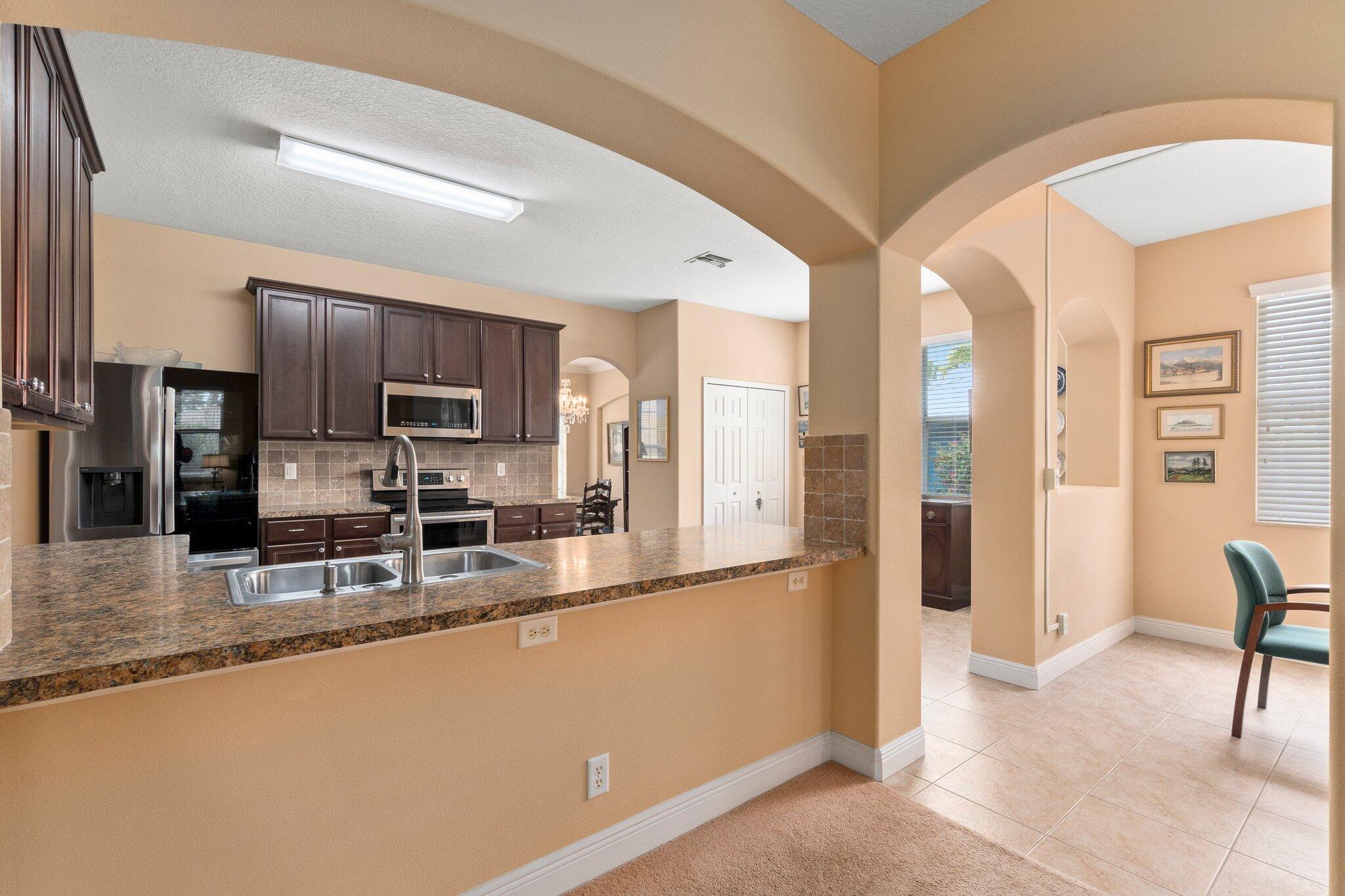 2309 Southwest Ivory Road Port St. Lucie, FL 34953 - Photo 14 of 46 a kitchen with stainless steel appliances granite countertop a refrigerator a stove a sink a dining table and chairs with wooden floor