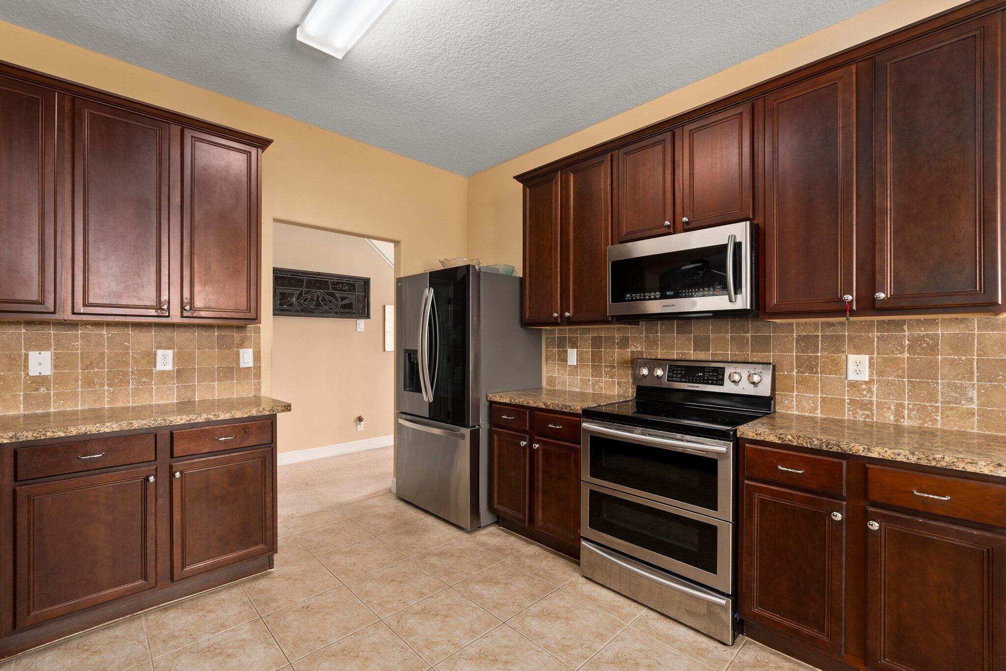 2309 Southwest Ivory Road Port St. Lucie, FL 34953 - Photo 10 of 46 a kitchen with granite countertop wooden cabinets stainless steel appliances and a granite counter tops