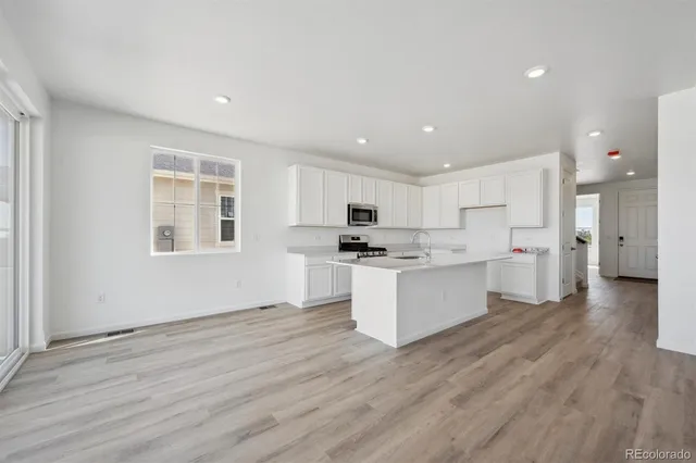 a view of kitchen with granite countertop refrigerator oven sink and white cabinets with wooden floor