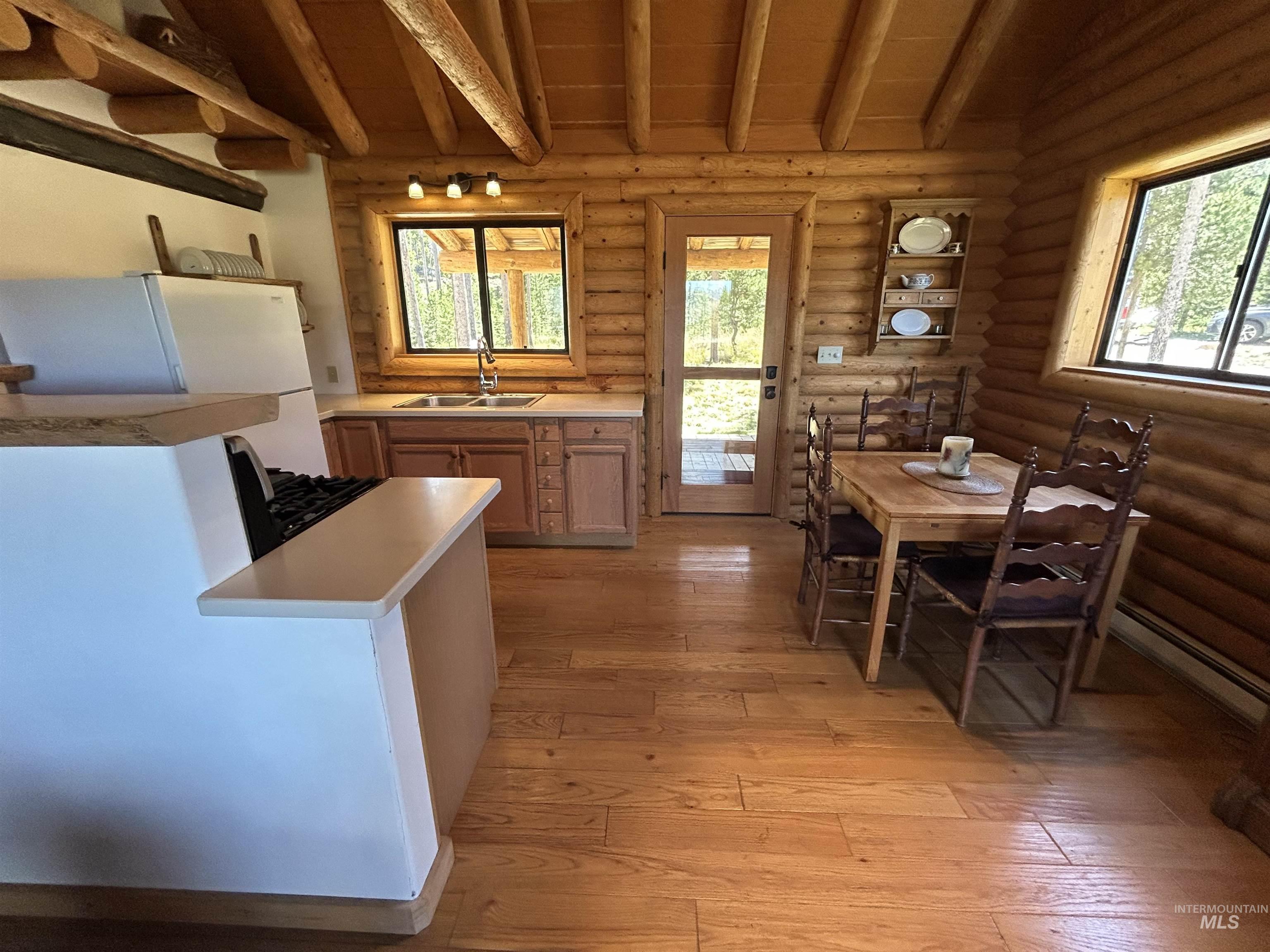35 Sawtooth Way Stanley, ID 83278 - Photo 12 of 36 Open-concept kitchen and dining area featuring rich wood-finish flooring, exposed log walls, natural wood cabinetry, and a double basin sink