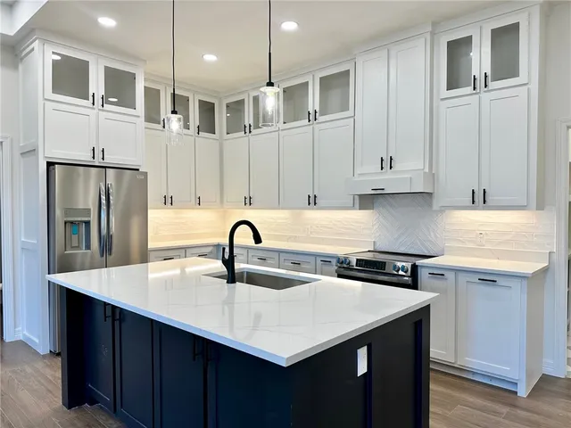 a kitchen with stainless steel appliances granite countertop a sink a refrigerator and white cabinets